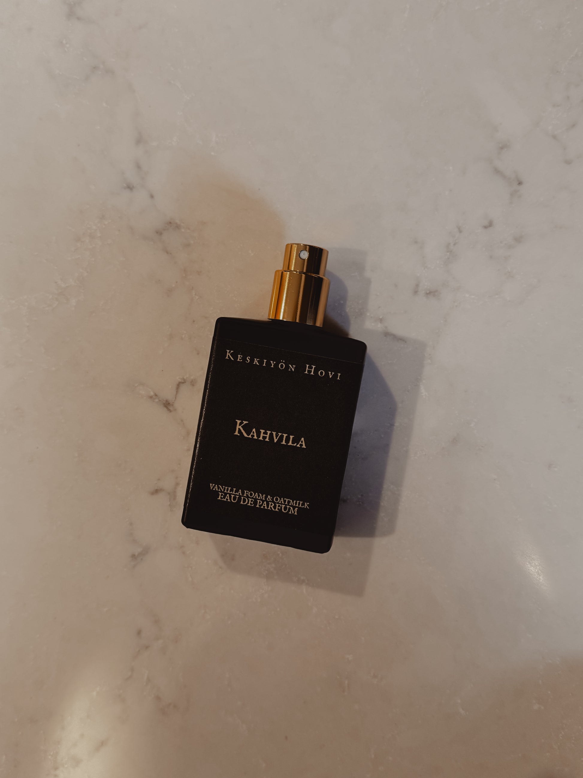 Black perfume bottle labeled 'Kahvila' on a marble surface