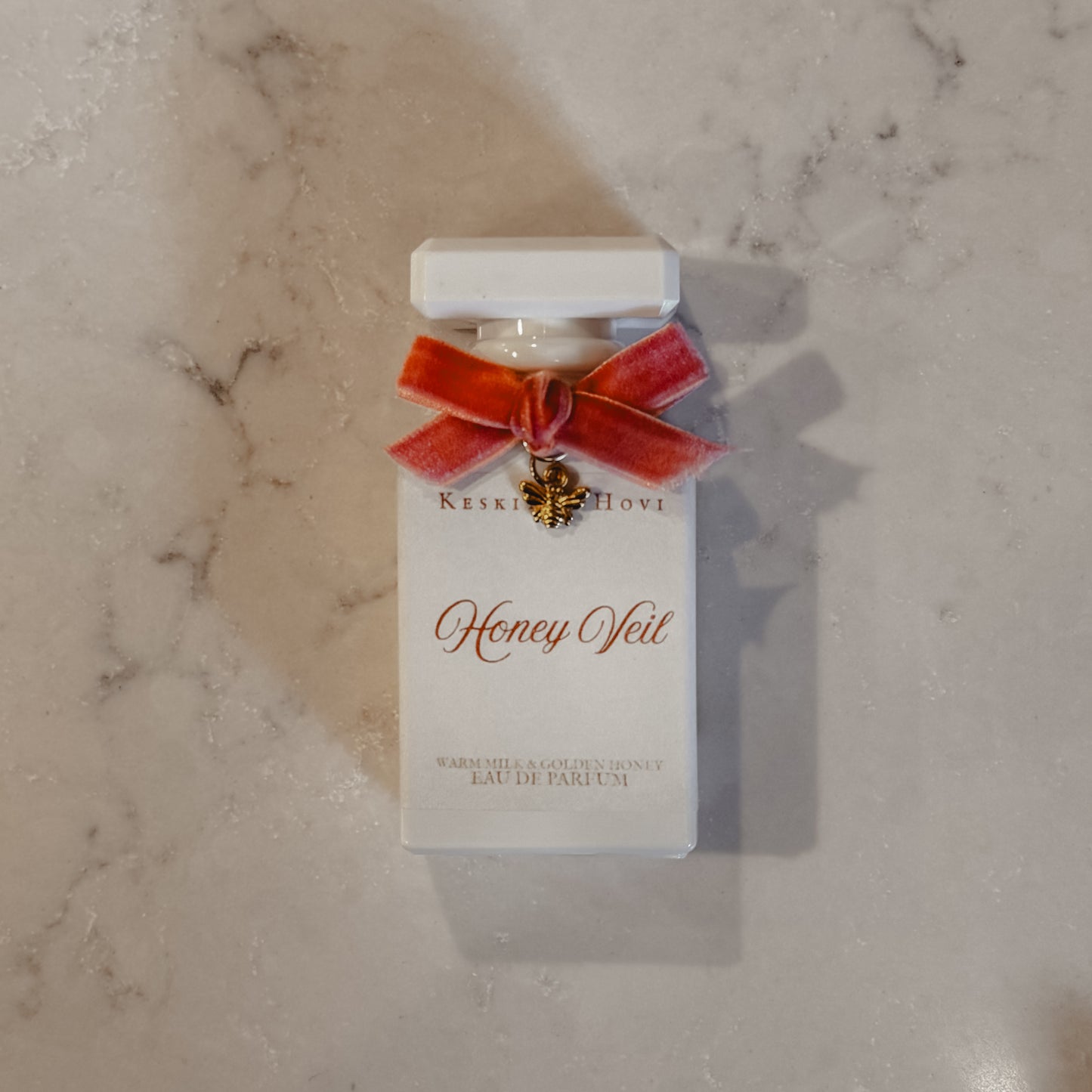 Perfume bottle labeled 'Honey Veil' with a red bow on a marble surface
