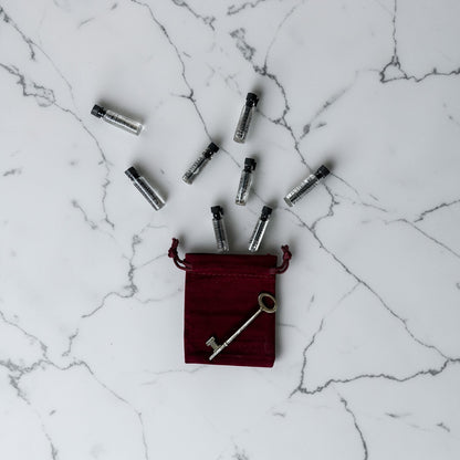 Red velvet pouch with a key and small silver bottles on a marble surface