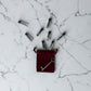 Red velvet pouch with a key and small silver bottles on a marble surface