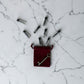 Red velvet pouch with a key and small silver bottles on a marble surface