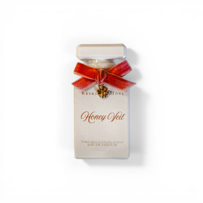 Perfume bottle with a red bow and bee charm on a white background