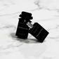 Two black perfume bottles labeled 'Crown of Ash' and 'Poisoned Vow' on a marble surface.