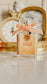 Perfume bottle with a pink bow and decorative elements on a reflective surface.