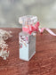 Perfume bottle with floral design and pink bow on a wooden surface