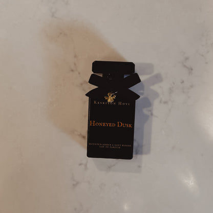 Black perfume bottle packaging with 'Honeyed Dusk' on a marble surface