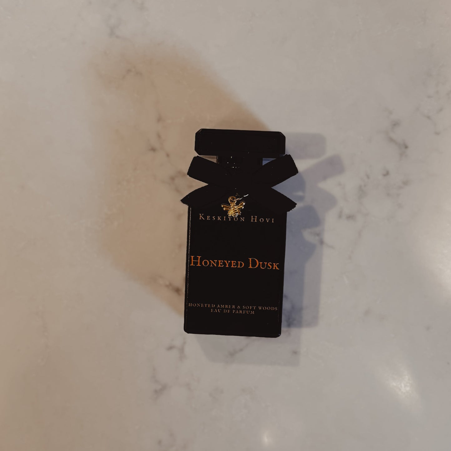 Black perfume bottle packaging with 'Honeyed Dusk' on a marble surface