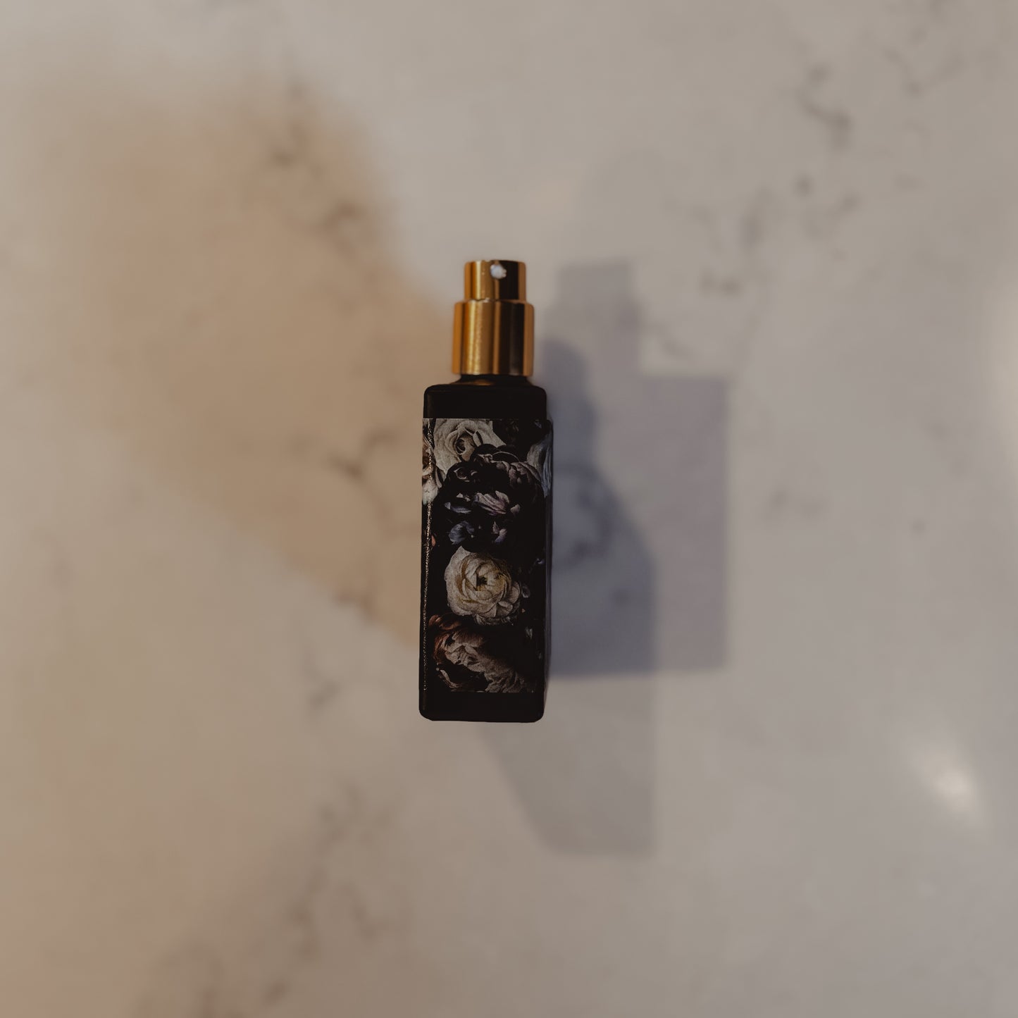 Black spray bottle with floral design on a marble surface
