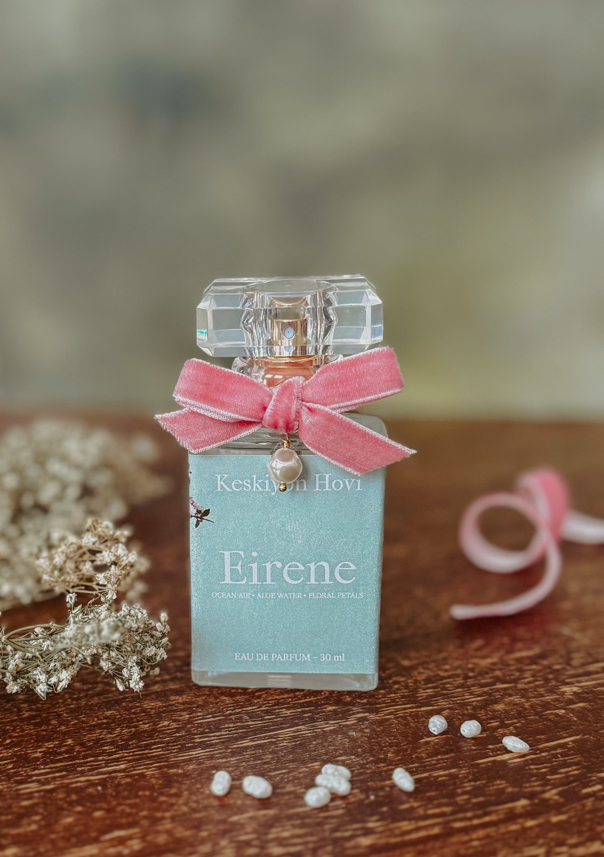 Perfume bottle with a pink bow labeled 'Eirene' on a wooden surface with dried flowers.