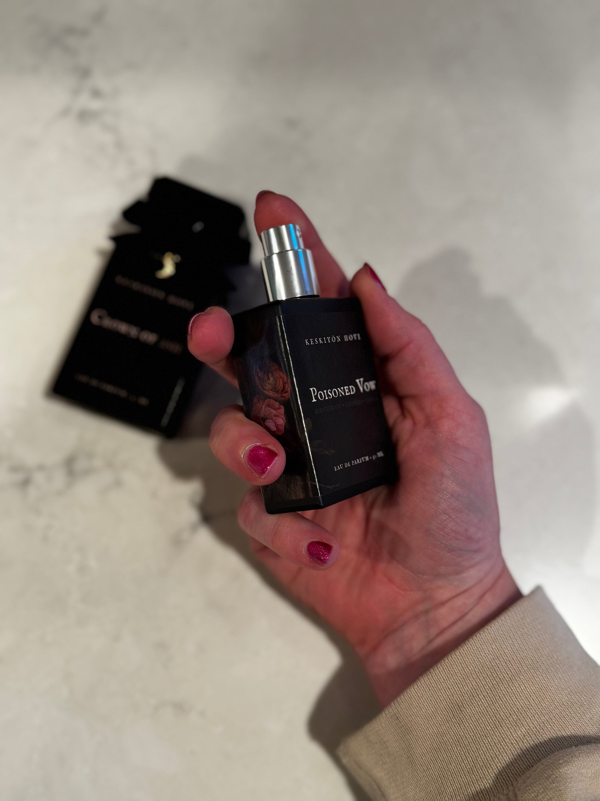 Hand holding a black perfume bottle labeled 'Pursued You' on a light marble surface.