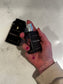 Hand holding a black perfume bottle labeled 'Pursued You' on a light marble surface.
