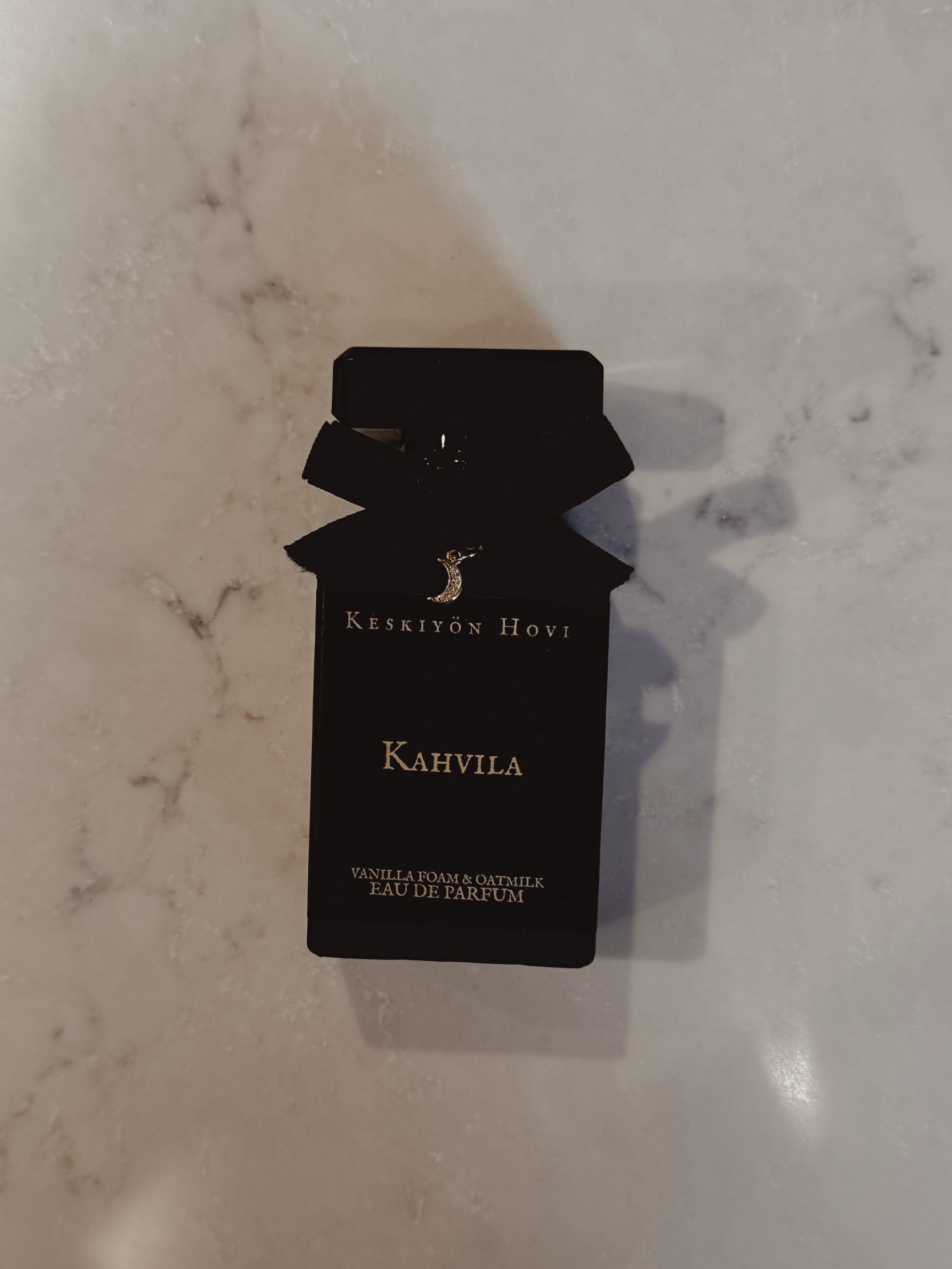 Black perfume bottle-shaped card with 'Keskivön Hovi' branding on a marble surface