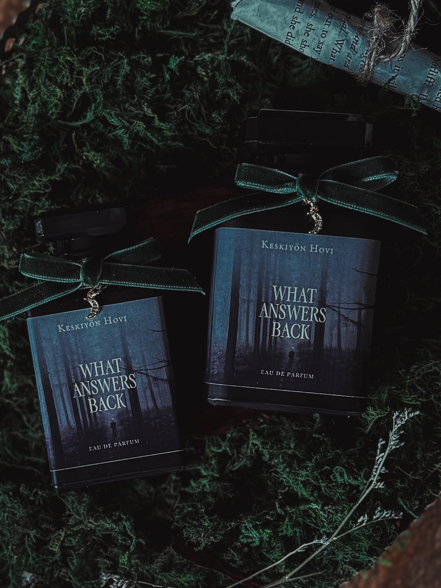 Two 'What Answers Back' perfume bottles with green ribbons on a textured surface.